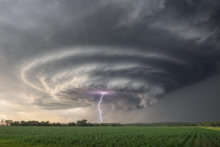 Supercell thunderstorm with a visible lightning strike over a green field